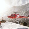 red helicopter flying over snow covered mountain during daytime