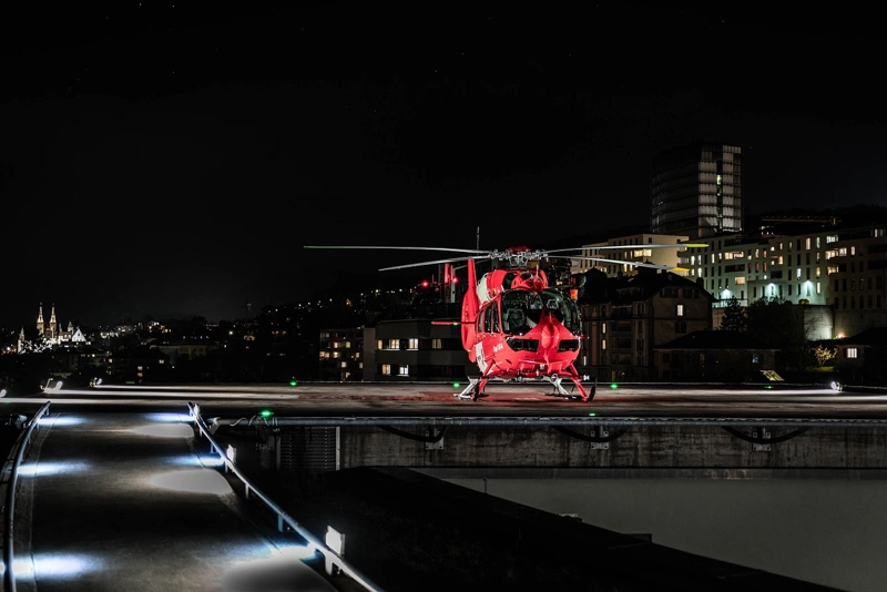 red helicopter on helipad at night with city lights in the background for travel emergency